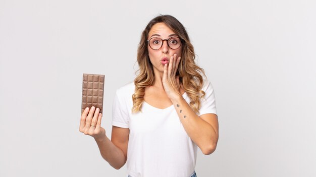 Mujer muy delgada sintiéndose conmocionada y asustada y sosteniendo una barra de chocolate