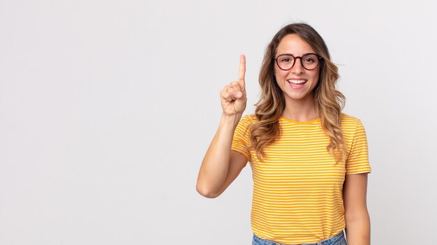 Mujer muy delgada sonriendo alegre y felizmente, apuntando hacia arriba con una mano para copiar el espacio