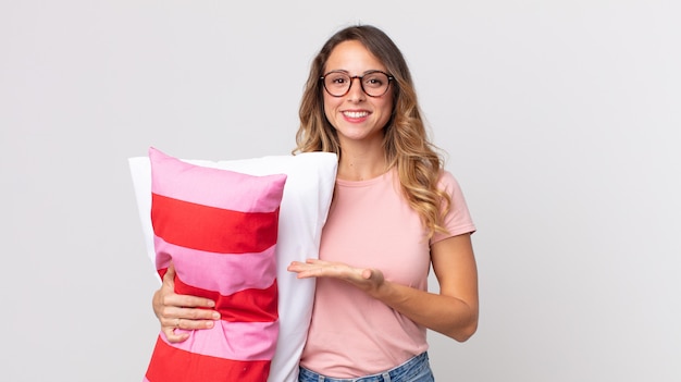 Mujer muy delgada sonriendo alegremente, sintiéndose feliz y mostrando un concepto vistiendo pijama y sosteniendo una almohada