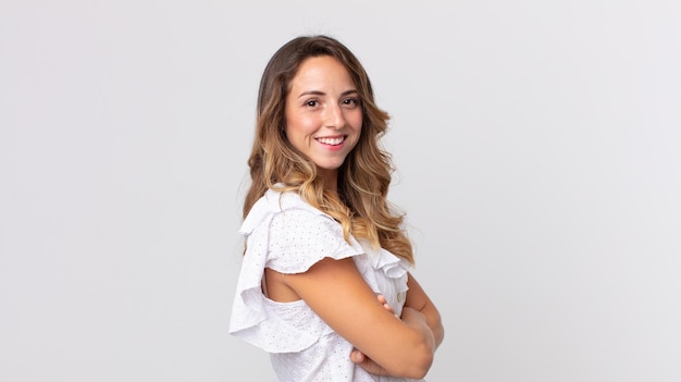 Foto mujer muy delgada sonriendo a la cámara con los brazos cruzados y una expresión feliz, confiada y satisfecha, vista lateral