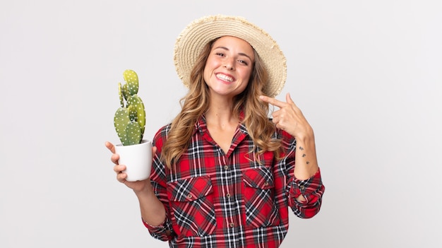 Mujer muy delgada sonriendo con confianza apuntando a su propia amplia sonrisa sosteniendo un cactus. concepto de granjero