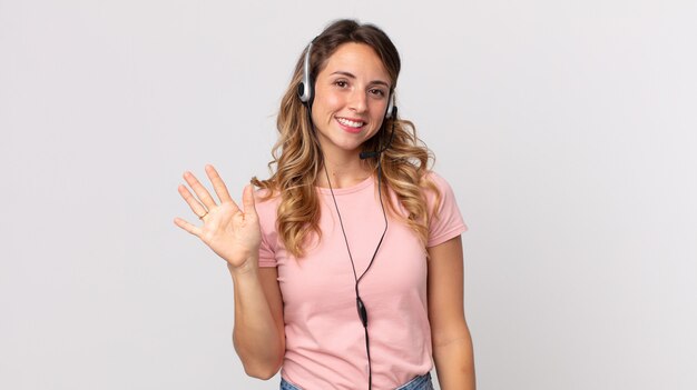 Mujer muy delgada sonriendo felizmente, saludando con la mano, dándole la bienvenida y saludándolo asistente del operador con un auricular