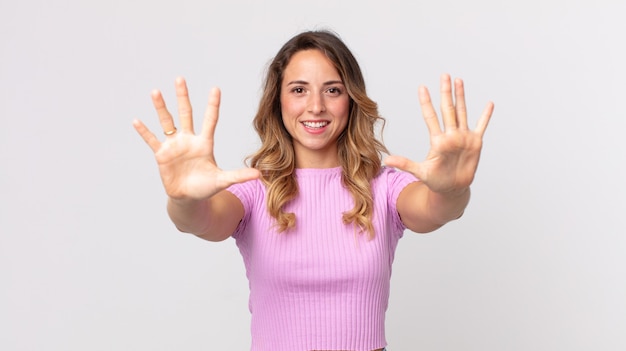 Mujer muy delgada sonriendo y mirando amigable, mostrando el número diez o décimo con la mano hacia adelante, contando hacia atrás