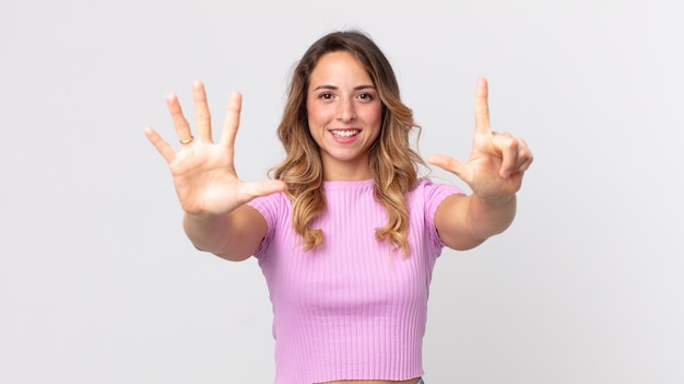 Foto mujer muy delgada sonriendo y mirando amigable, mostrando el número siete o séptimo con la mano hacia adelante, contando hacia atrás