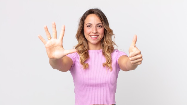 Mujer muy delgada sonriendo y mirando amistosamente, mostrando el número seis o sexto con la mano hacia adelante, contando hacia atrás