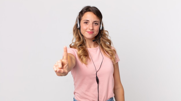 Mujer muy delgada sonriendo con orgullo y confianza haciendo asistente de operador número uno con un auricular