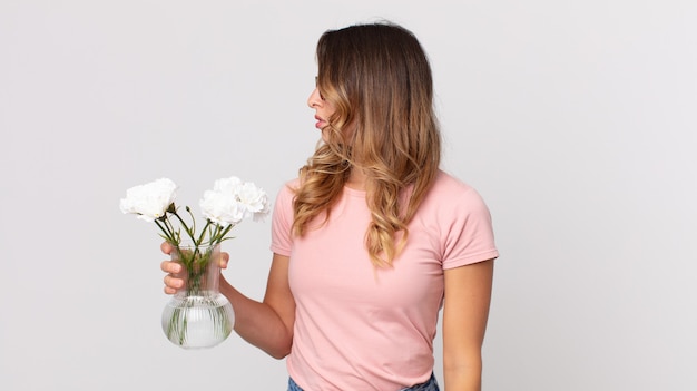 Mujer muy delgada en vista de perfil pensando, imaginando o soñando despierto y sosteniendo flores decorativas