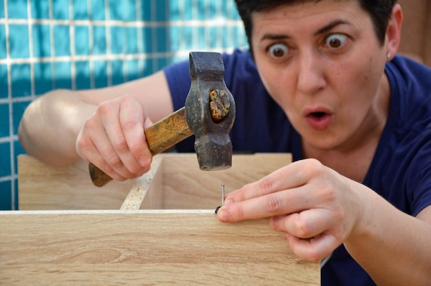 Mujer muy diligentemente martilla clavos con martillo, ensamblando muebles en el apartamento por su cuenta. Bricolaje