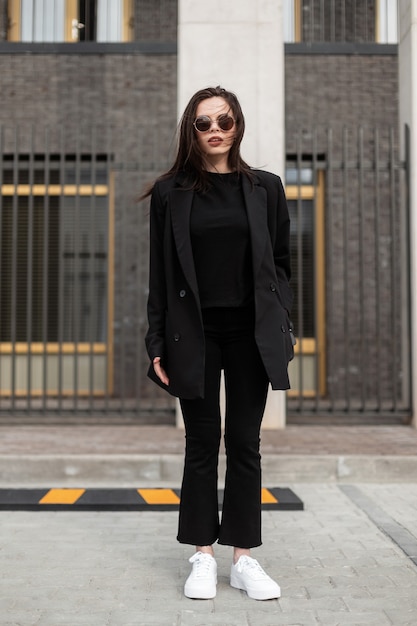 Chica en ropa juvenil casual negra de moda. mujer joven moderna en blazer  de moda en elegante camiseta negra se encuentra en la calle en la ciudad.  traje negro vintage para mujer.