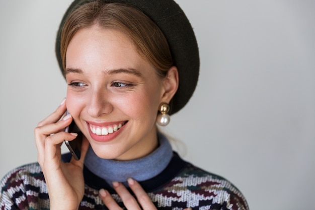 Mujer muy feliz con aretes sonriendo y hablando por teléfono celular aislado en blanco