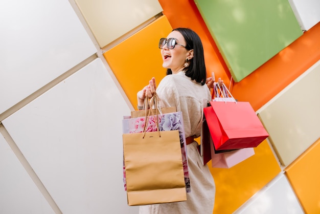 Foto mujer muy feliz con bolsas de compras posando en la pared de colores de la tienda