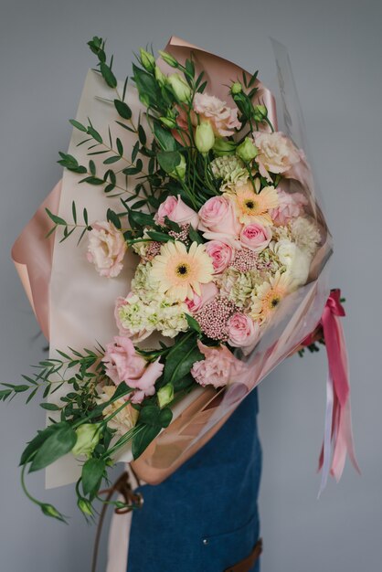 Mujer muy hermosa del florista que sostiene un ramo floreciente colorido hermoso de flores en un fondo gris de la pared.