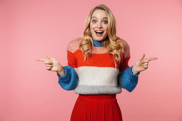 Una mujer muy hermosa joven emocionada feliz posando aislada sobre pared rosa apuntando a copyspace