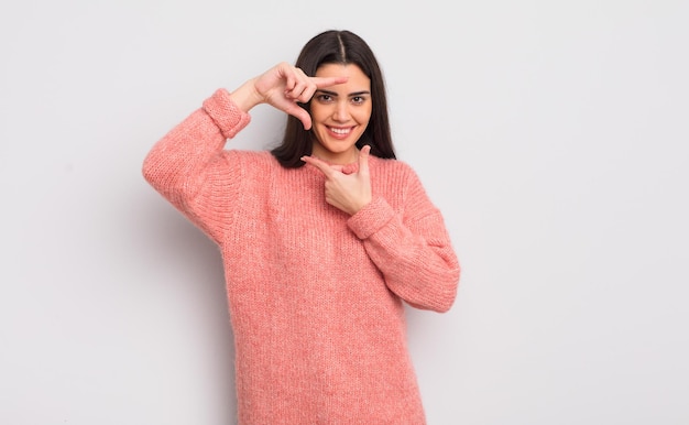 Mujer muy joven que se siente feliz, amistosa y positiva, sonriendo y haciendo un retrato o un marco de fotos con las manos