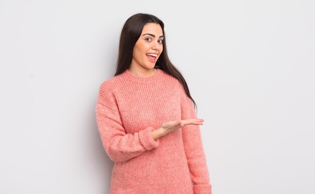 mujer muy joven sonriendo alegremente, sintiéndose feliz y mostrando un concepto en el espacio de copia con la palma de la mano