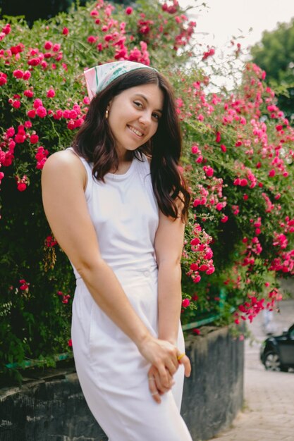 Mujer muy sonriente joven cerca del arbusto de rosas rojas en flor