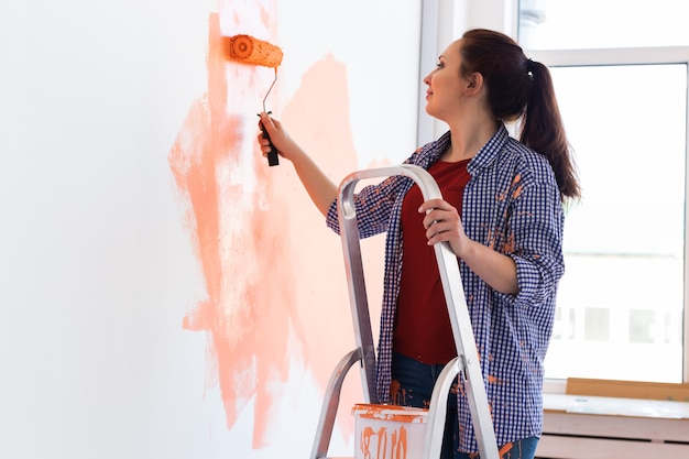 Mujer muy sonriente pintando la pared interior de la casa con rodillo de pintura. Redecoración, renovación