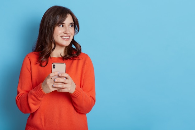 Mujer muy sonriente sosteniendo un teléfono inteligente, mira hacia otro lado con expresión alegre