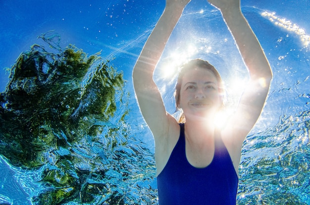La mujer nada bajo el agua en la piscina, una niña activa y saludable se sumerge y se divierte bajo el agua, hace ejercicio y practica deporte en sus vacaciones