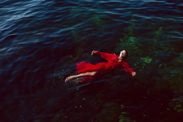 Mujer nada en el mar con un vestido largo rojo con gafas de sol en verano