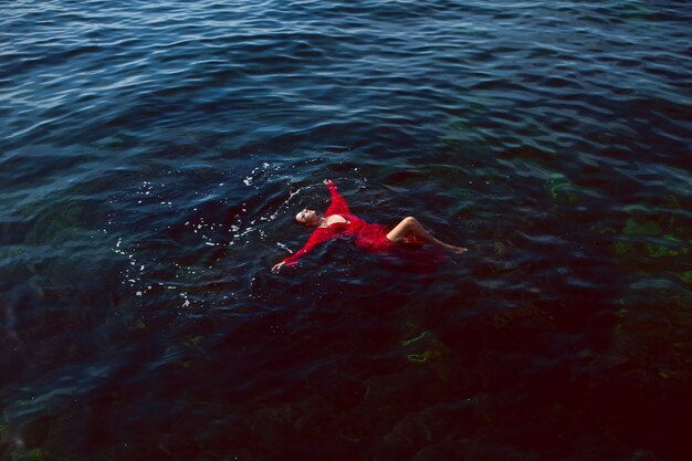 Mujer nada en el mar con un vestido largo rojo con gafas de sol en verano