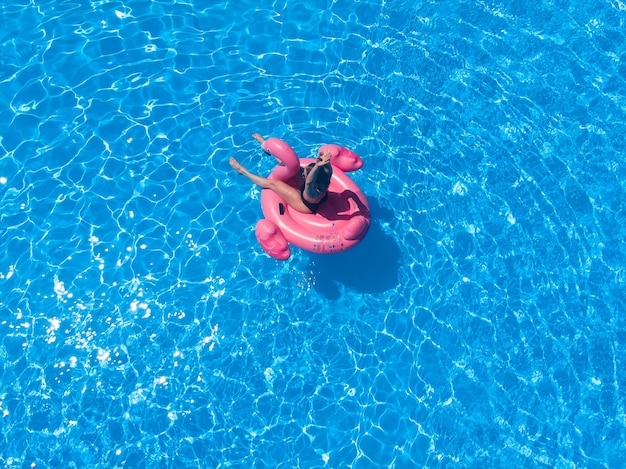 Mujer nadando con flamnigo rosa en la piscina vista desde arriba, vista aérea superior desde drone, relajación de verano en el hotel