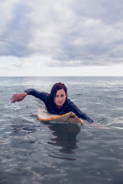 Foto mujer nadando sobre la tabla de surf en el agua