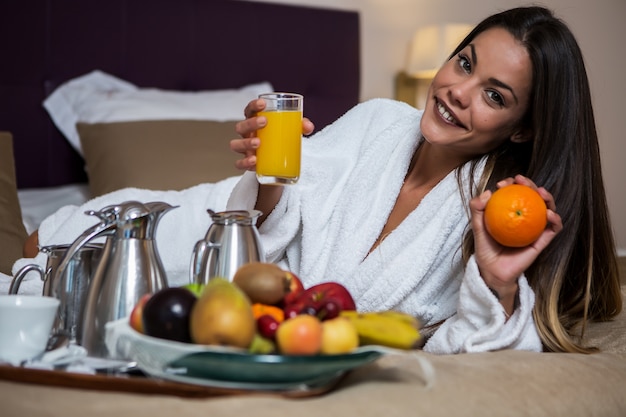 Mujer con naranja y vaso de jugo mirando a cámara