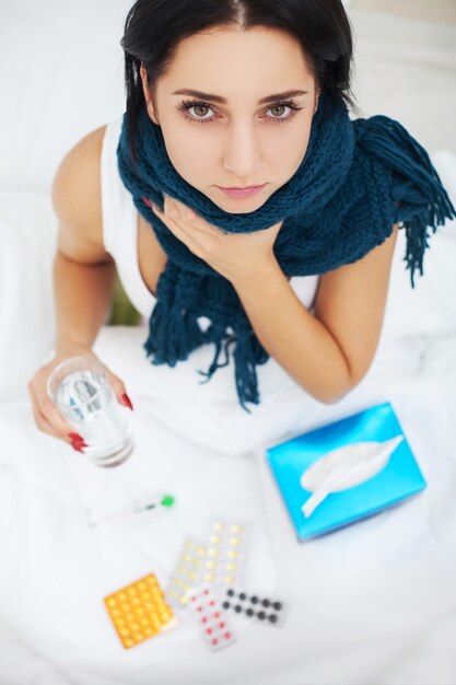 Mujer con nariz estornudando con pañuelo en la cama que sufre el virus de la gripe fría con medicamentos
