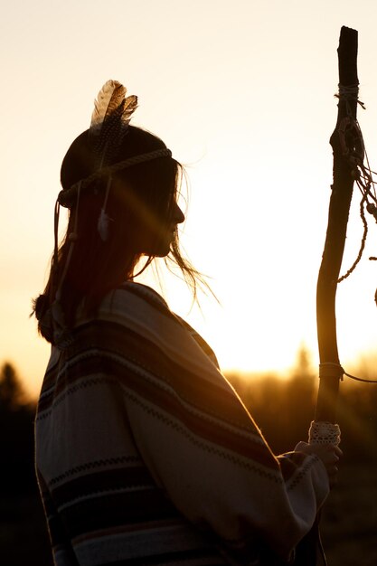 Foto mujer nativa americana chamán con pikestaff en el fondo de la hermosa puesta de sol en las montañas