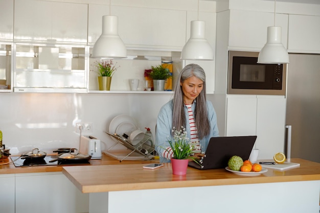 Mujer navegando por internet en la computadora portátil en la cocina