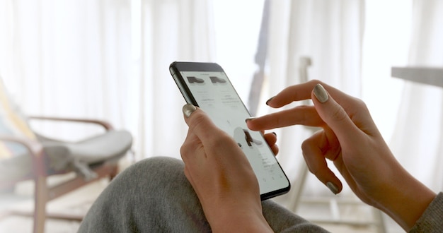 Mujer navegando por la pantalla del teléfono inteligente pidiendo ropa en casa en línea