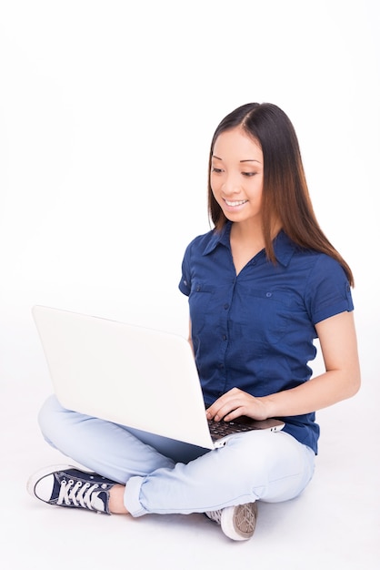 Mujer navegando por la red. Alegre joven asiática trabajando en equipo portátil y sonriendo