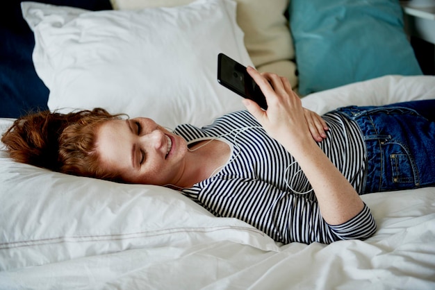 Mujer navegando por el teléfono móvil mientras está acostada en la cama