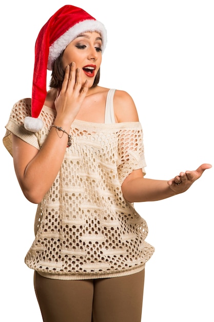 Mujer de Navidad que muestra la palma vacía con espacio de copia sonríe sorprendentemente de pie. Mujer sonriente joven hermosa en el sombrero rojo de Santa que muestra el copyspace.