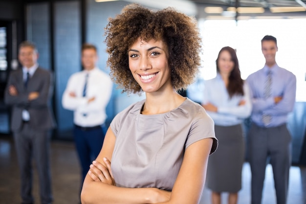 Mujer de negocios acertada que sonríe mientras que sus colegas que se colocan detrás de él en oficina