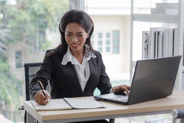 Mujer de negocios africana que trabaja en la oficina usando una computadora y escribiendo en un cuaderno