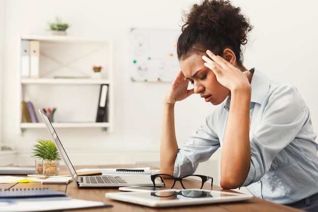 Mujer de negocios afroamericana cansada con dolor de cabeza en la oficina, malestar en el trabajo, espacio de copia