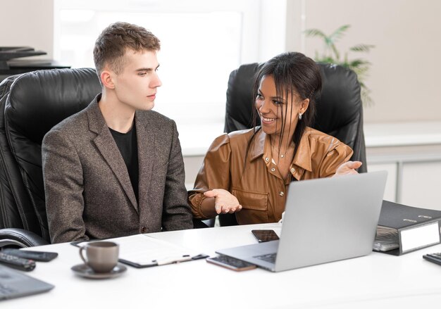 Mujer de negocios afroamericana en el cargo con un joven colega que trabaja en una laptop