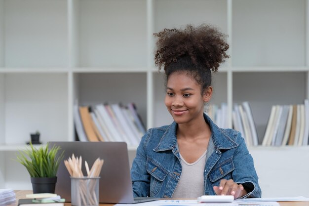 Mujer de negocios afroamericana con una chaqueta de jeans sentada y usando una computadora portátil en una oficina