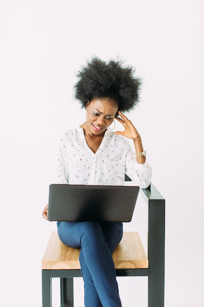 Mujer de negocios afroamericana joven alegre concentrada y confundida, usando la computadora portátil, aislada en blanco