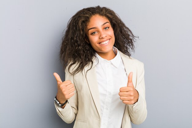 Mujer de negocios afroamericana joven levantando ambos pulgares, sonriente y confiado.