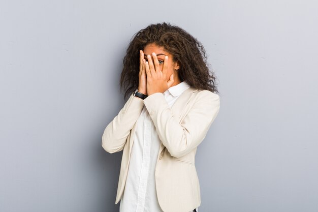 La mujer de negocios afroamericana joven parpadea entre los dedos asustada y nerviosa.