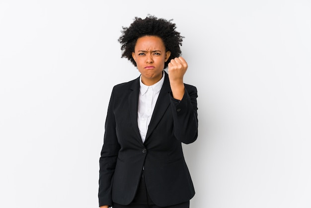 Mujer de negocios afroamericana de mediana edad contra una pared blanca aislada mostrando el puño con expresión facial agresiva.