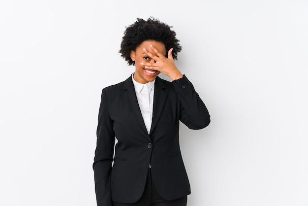 Mujer de negocios afroamericana de mediana edad contra una pared blanca aislada parpadear a la cámara a través de los dedos, avergonzado cubriendo la cara.