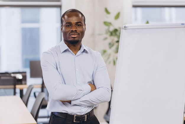 Mujer de negocios afroamericana profesional de pie cerca de un cuadro en blanco preparándose para una presentación estratégica en un elegante espacio de trabajo corporativo