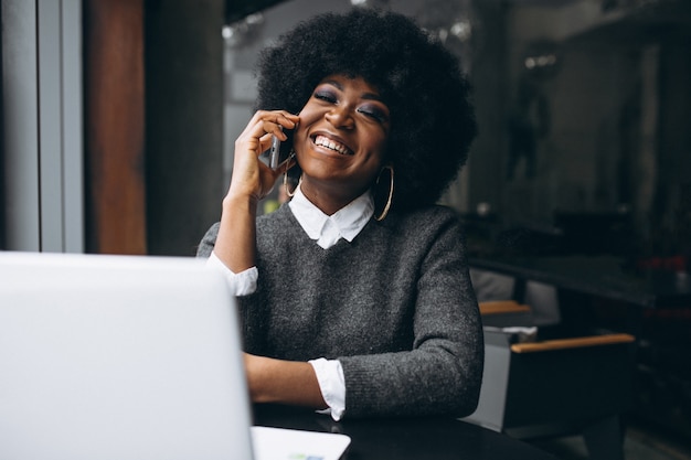 Mujer de negocios afroamericana que trabaja en la computadora portátil en un café