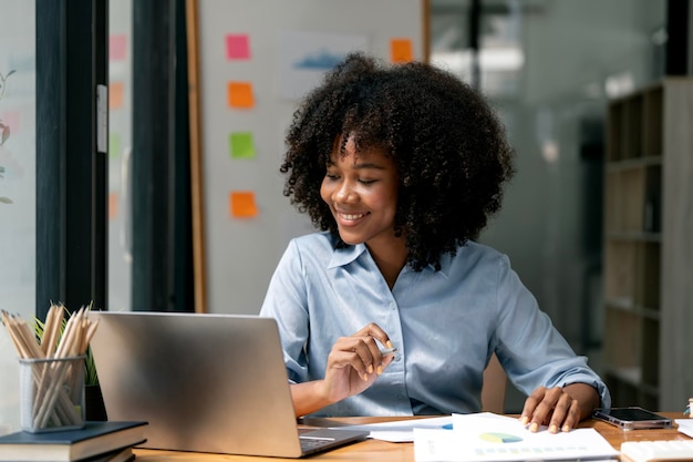 Mujer de negocios afroamericana que trabaja dentro de la oficina con documentos y una computadora portátil sonriendo y feliz con el éxito y los resultados de los logros