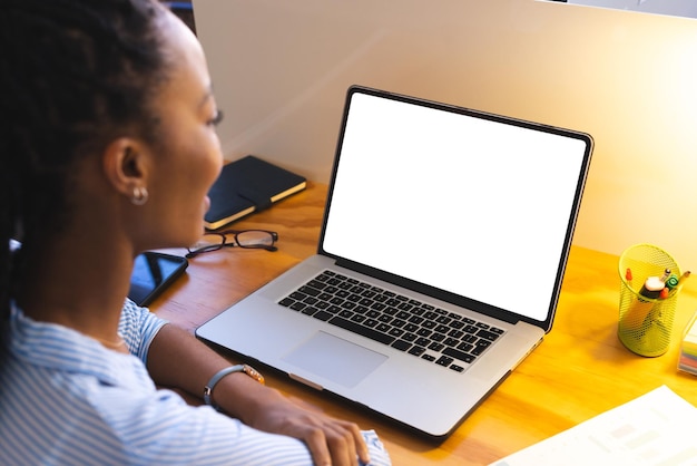 Una mujer de negocios afroamericana que usa una computadora portátil con espacio de copia en la pantalla en la oficina. Oficina casual, negocios, comunicación y trabajo, sin alteraciones.