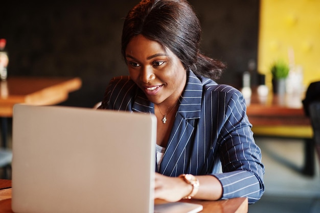 Mujer de negocios afroamericana sentada en la mesa en el café Chica negra trabajando con una computadora portátil